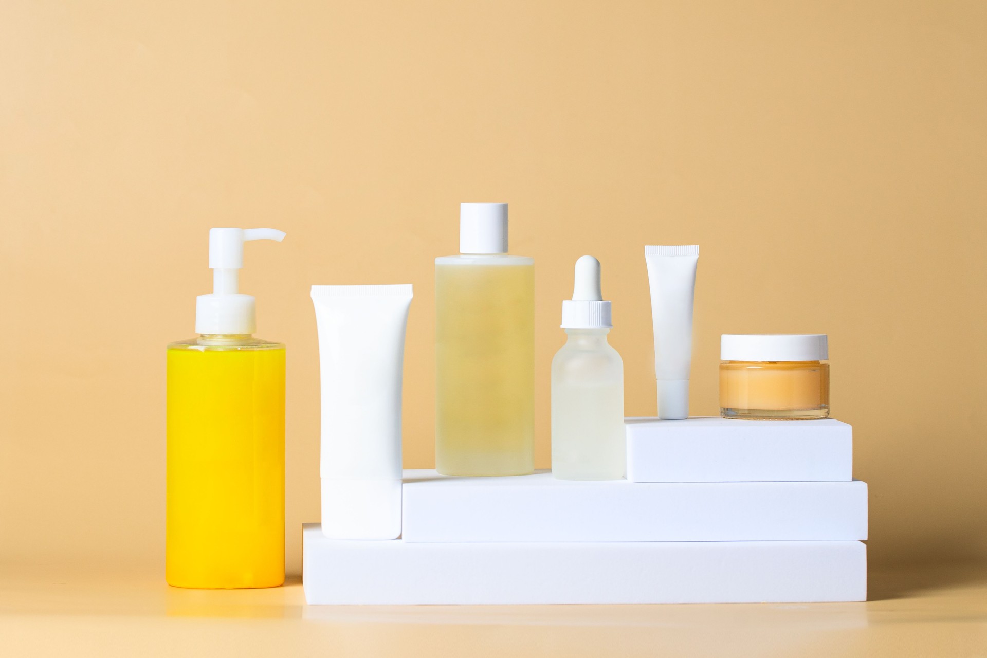 Different skincare product set. Fcial cleanser, toner, essence, serum, cream on white podium beige background. Beauty salon and cosmetic shop