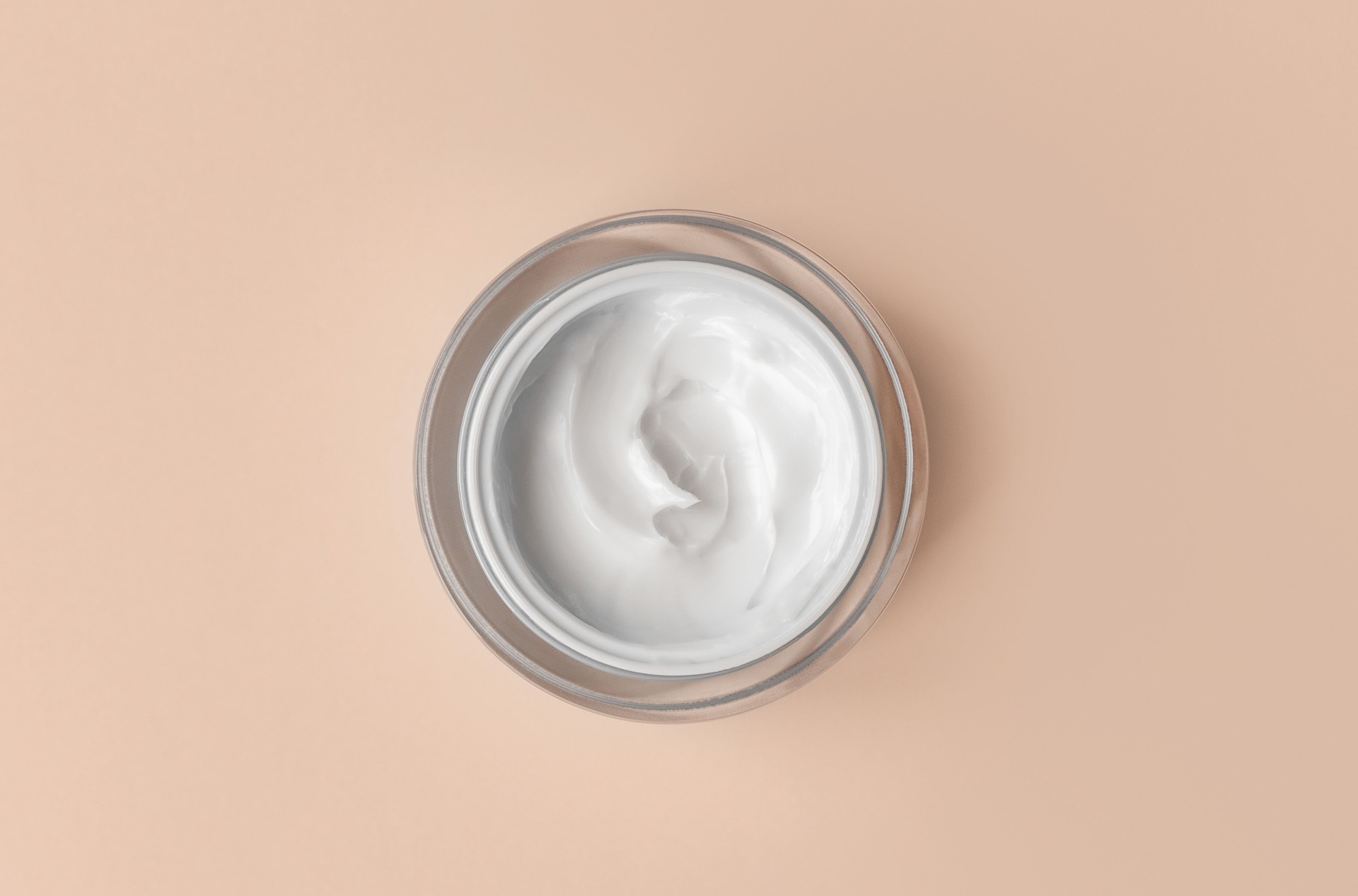 White cream jar on beige background close-up. Beauty cosmetics presentation. Top view