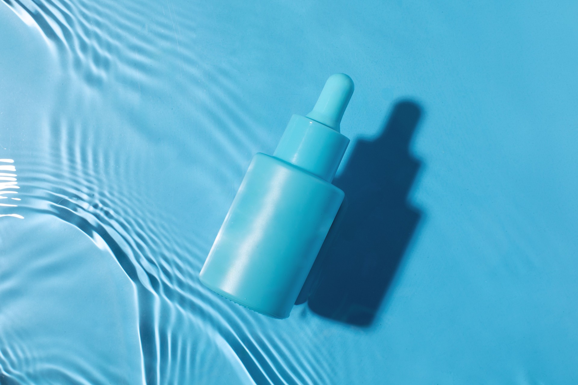Blue serum bottle on water surface. Face serum mockup. Beauty concept.